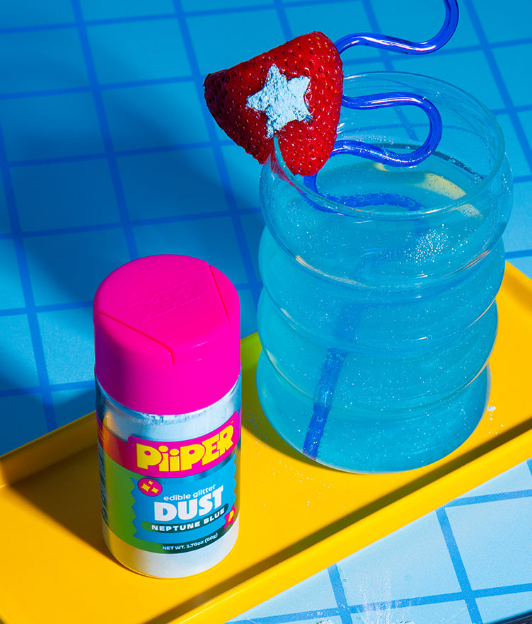 Front view of PiiPER Edible Glitter Dust - Neptune Blue shaker showcasing glitter in a blue drink and on a strawberry