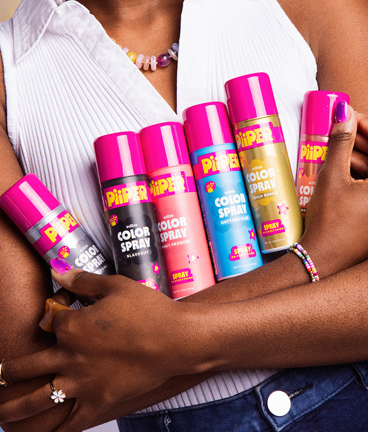 Front view of PiiPER Edible Color Spray Pinky Promise can among colorful sprays held against a white pleated shirt