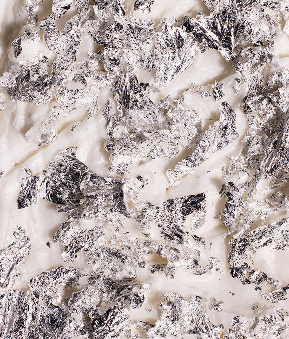 Close-up of edible real silver leaf flakes showcasing reflective metallic texture on a white surface