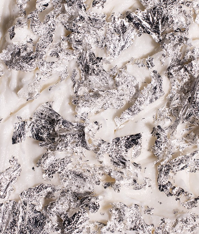Close-up of real silver edible flakes showcasing crinkled metallic texture on a white background