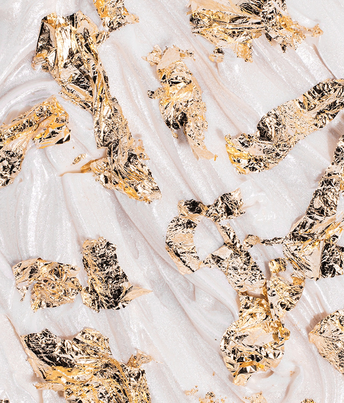 Close-up of gold decorative flakes showcasing reflective irregular pieces on a white textured background