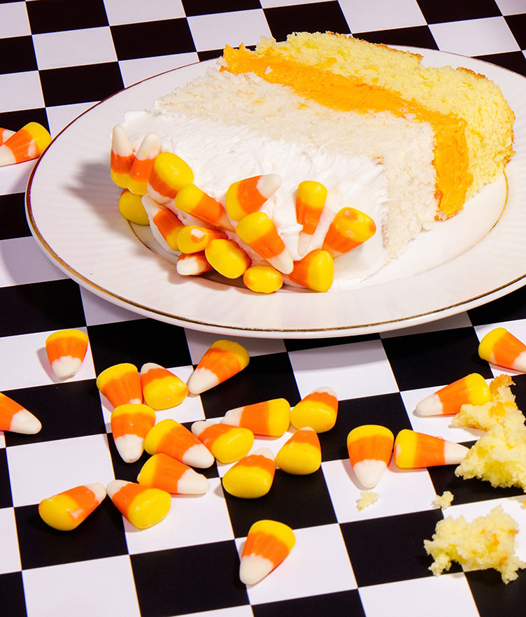 Candy corn buttercream frosting coats a cake slice surrounded by candy corn on a checkerboard table