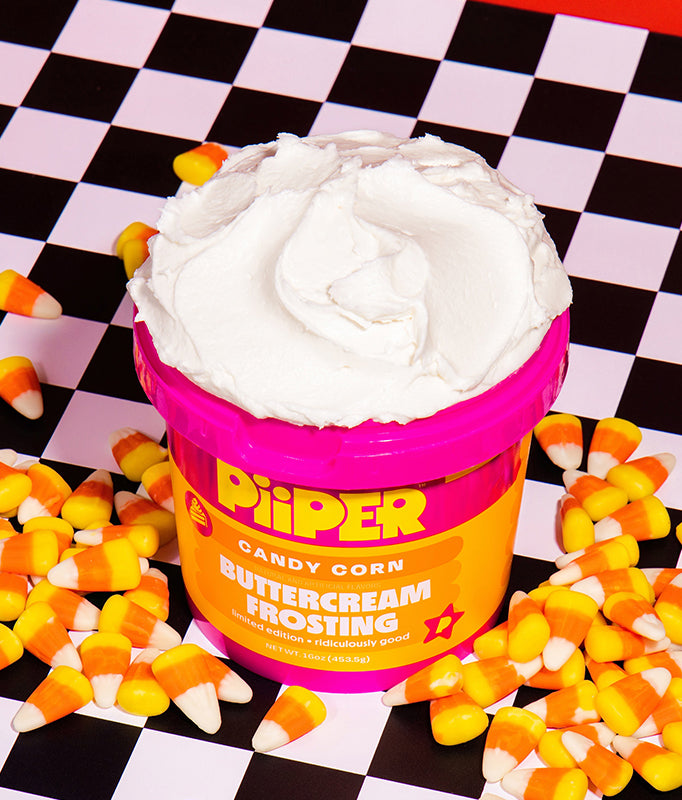 Front view of open PiiPER Candy Corn buttercream frosting tub showcasing white frosting with candy corn and checkerboard background