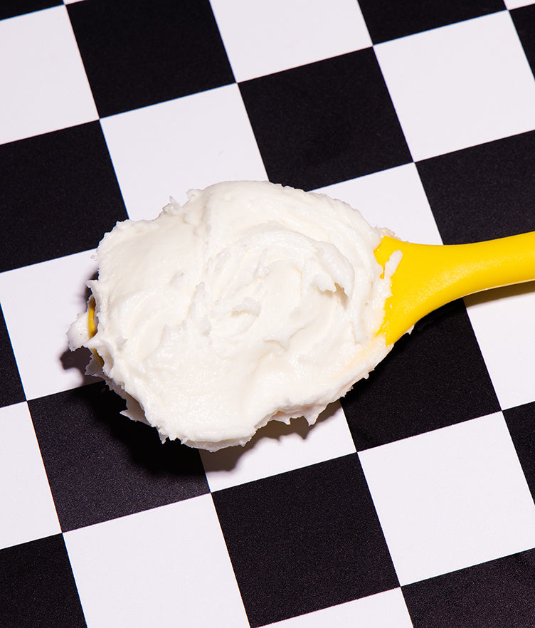 Close-up of Candy Corn buttercream frosting on a yellow spoon with a black-and-white checkerboard background