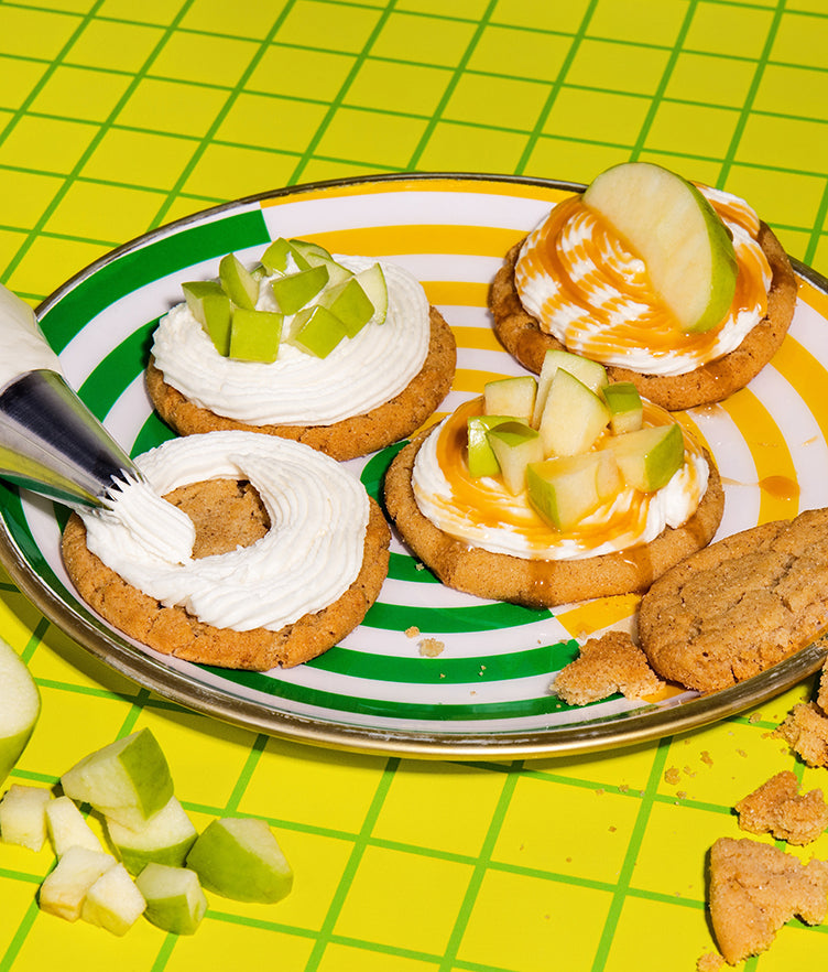 Caramel Apple buttercream frosting piped and spread on cookies with apple pieces and caramel drizzle on a plate