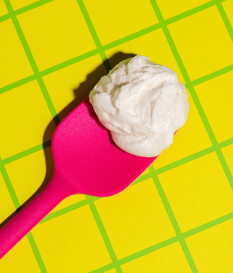 Close-up of Caramel Apple buttercream frosting on a pink spatula, showing its fluffy texture over a yellow-green grid