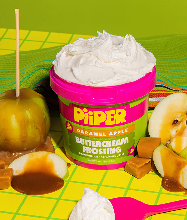 Front view of PiiPER Caramel Apple Buttercream Frosting with white frosting, caramel apples and candies on green