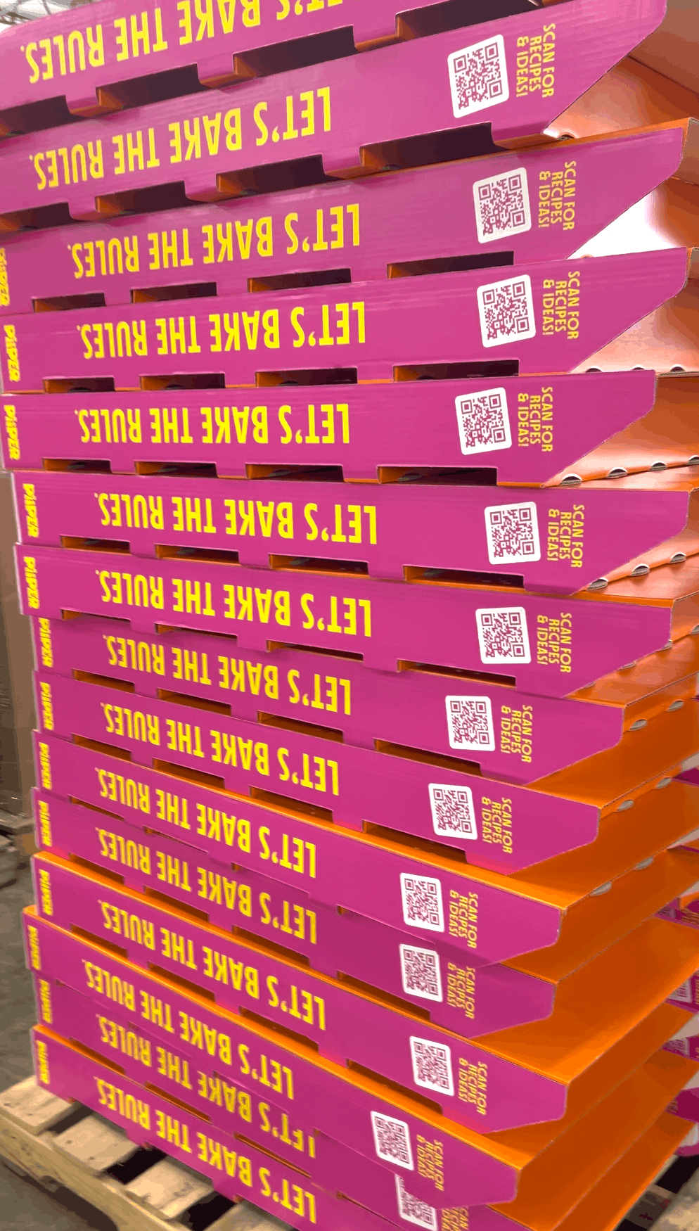 Close view of stacked pink and orange PiiPER display boxes with Let’s Bake the Rules text and recipe QR codes