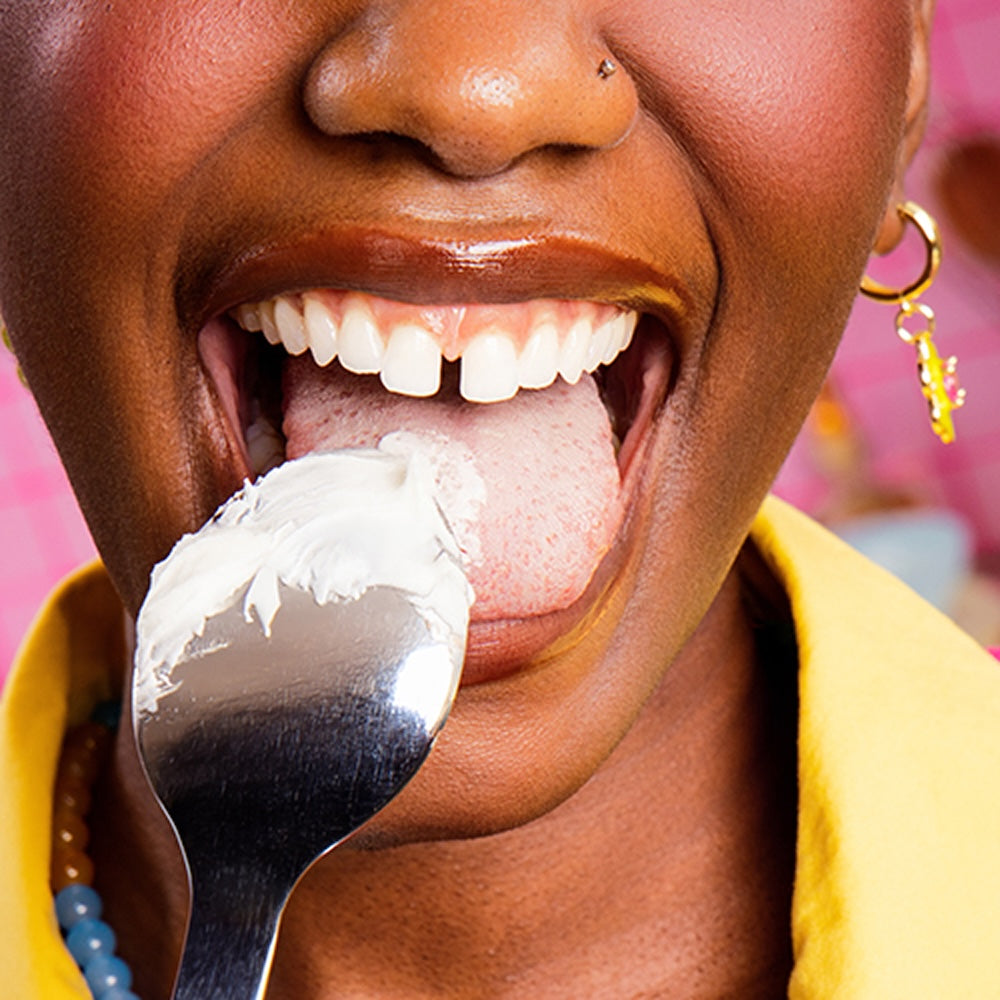Close-up of a person licking white frosting from a spoon while wearing a yellow jacket