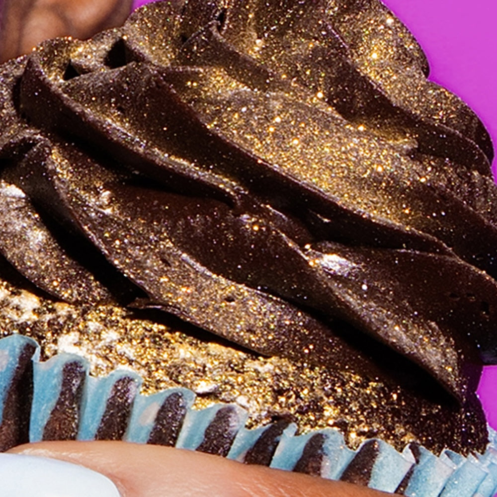 Close-up of a chocolate dessert showcasing gold glitter and blue frosting against a bright pink background