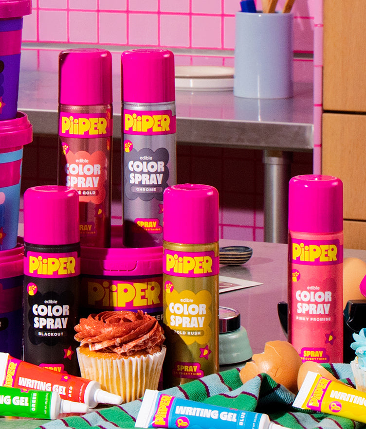 Front view of PiiPER edible Color Spray Blackout can with colorful sprays, writing gels, and a cupcake on a kitchen counter