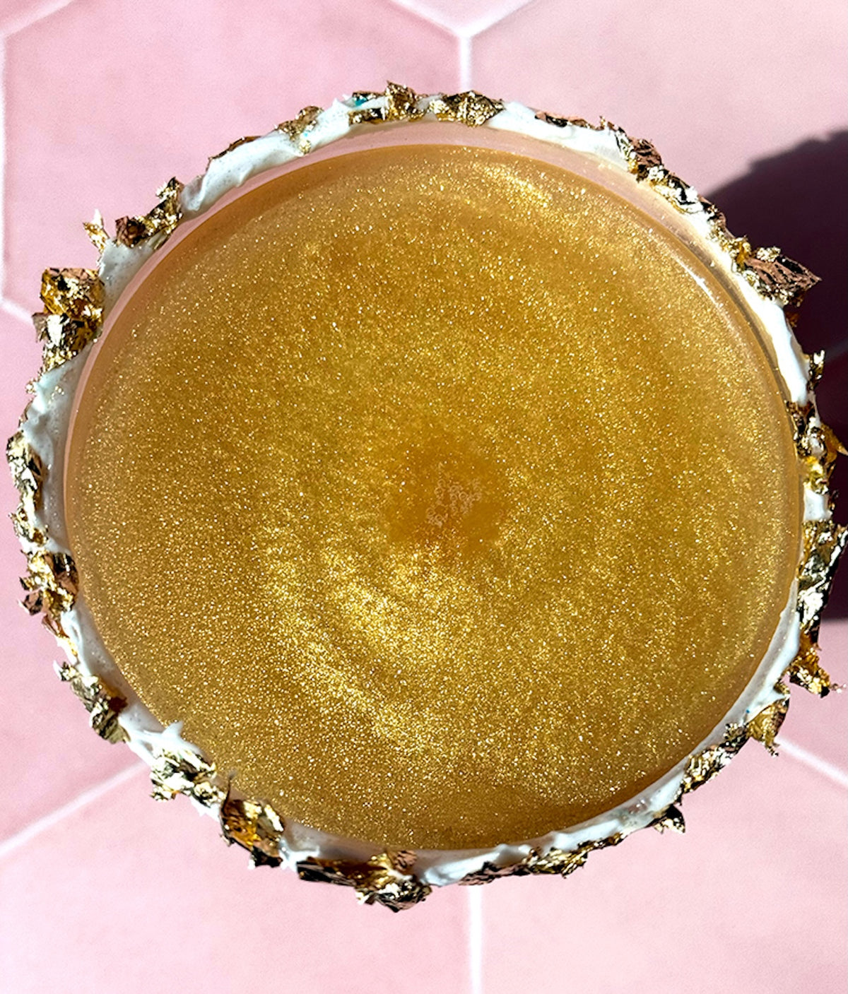 Top view of gold leaf flakes decorating a round dessert, showcasing crinkled metallic texture against a pink background