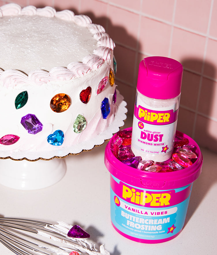 Front view of PiiPER 50g Edible Glitter Dust Diamond White shaker beside a decorated cake and frosting tub