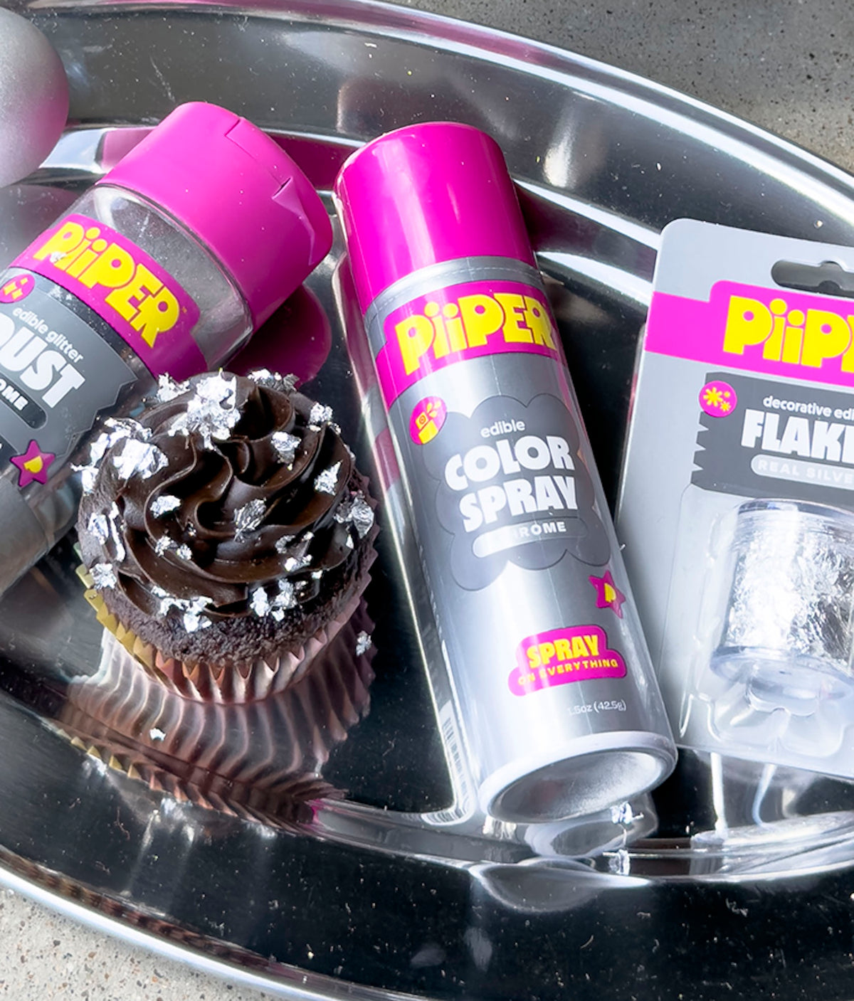 Close-up of PiiPER edible Color Spray in Chrome beside a decorated chocolate cupcake on a silver tray