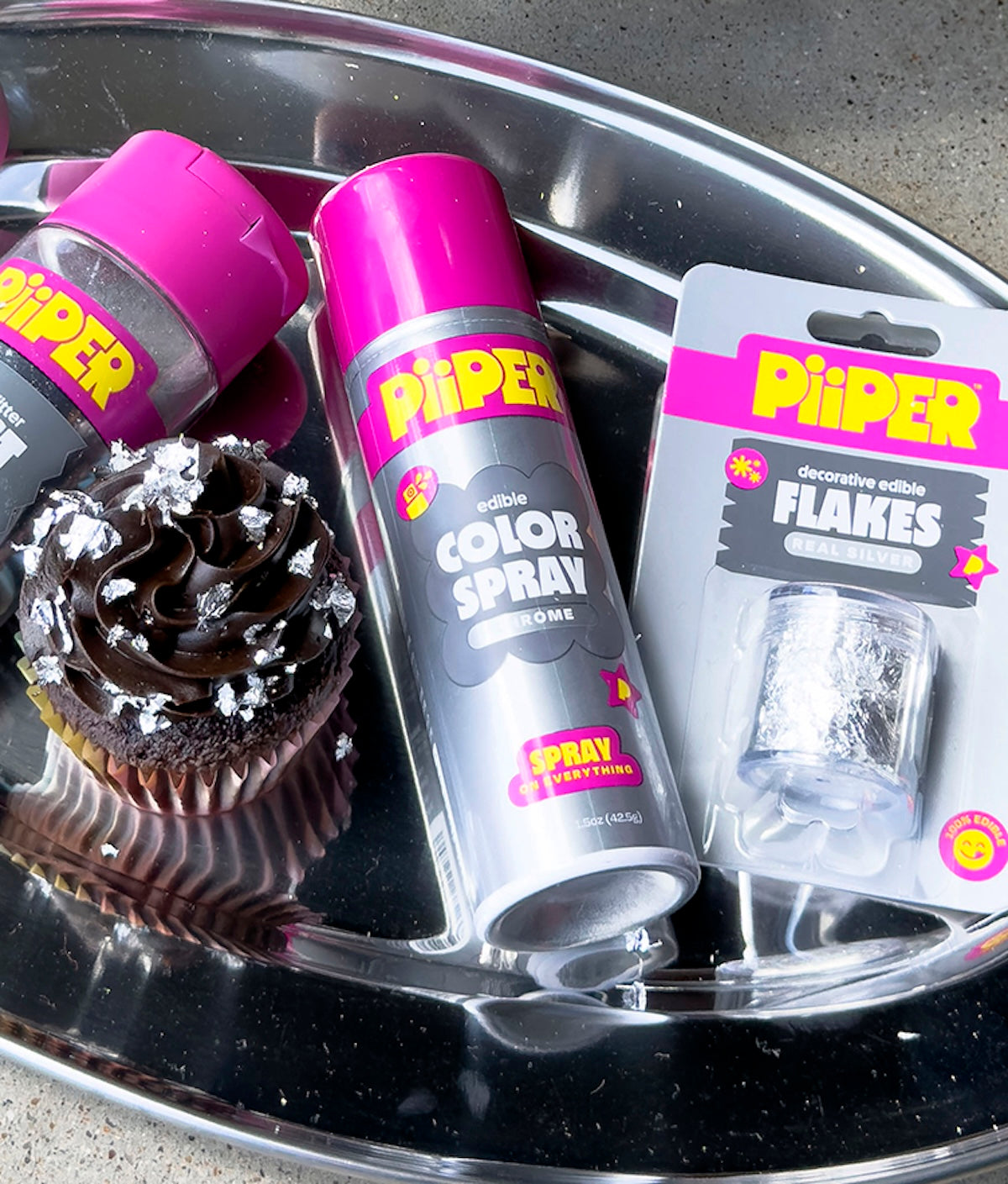 Close-up of PiiPER Decorative Edible Flakes – Real Silver jar with silver flakes, cupcake, and spray on a tray