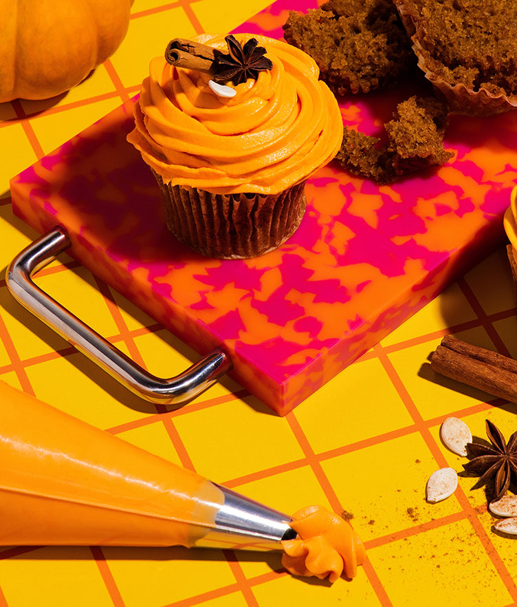 Pumpkin chai buttercream frosting piped onto a cupcake with pumpkin and chai spices nearby