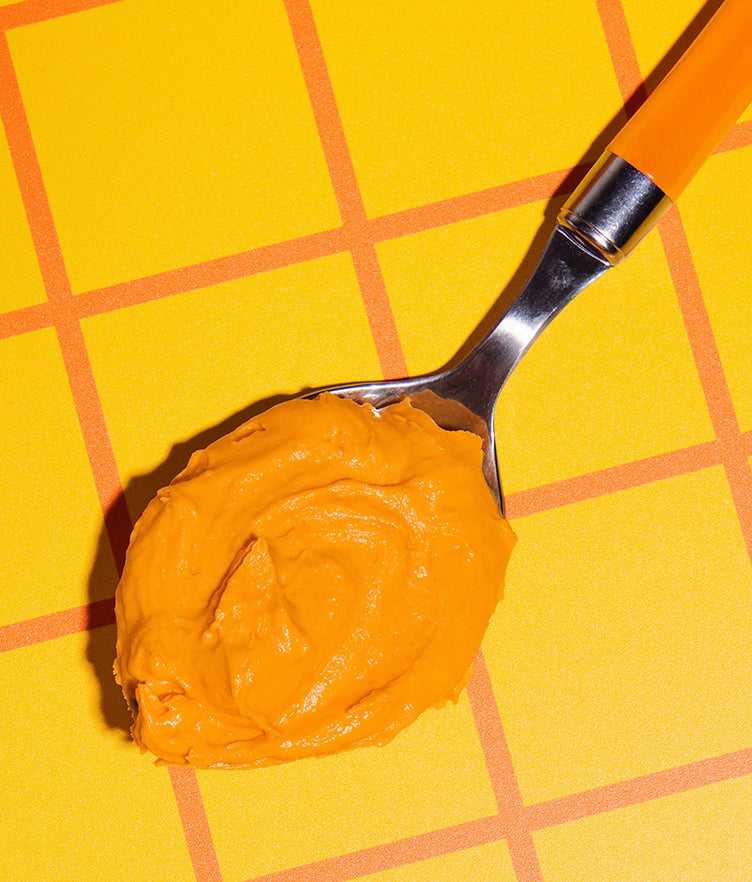 Close-up of Pumpkin Chai Buttercream Frosting on a spoon showcasing fluffy texture on a yellow-orange checkered background
