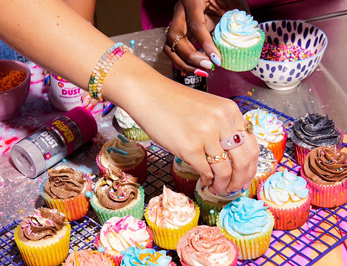 Hands decorating colorful cupcakes with PiiPER glitter dust and sprinkles