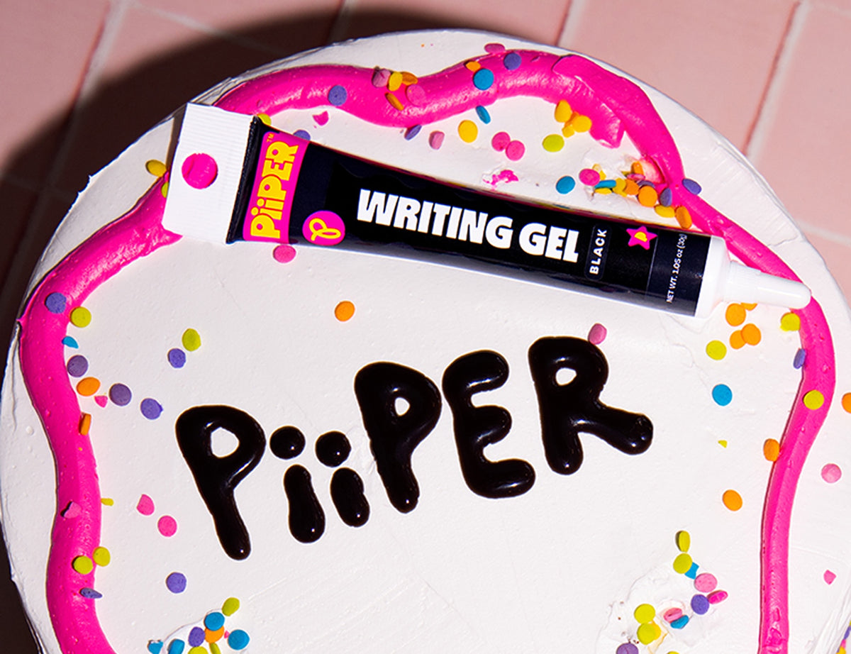 Angled view of PiiPER Writing Gel in black showcasing the tube packaging on a colorful frosted cake with sprinkles