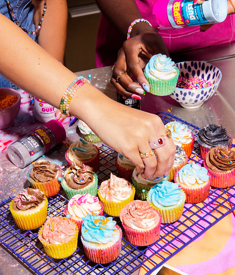 People decorate colorful frosted cupcakes with PiiPER edible glitter dust in a kitchen