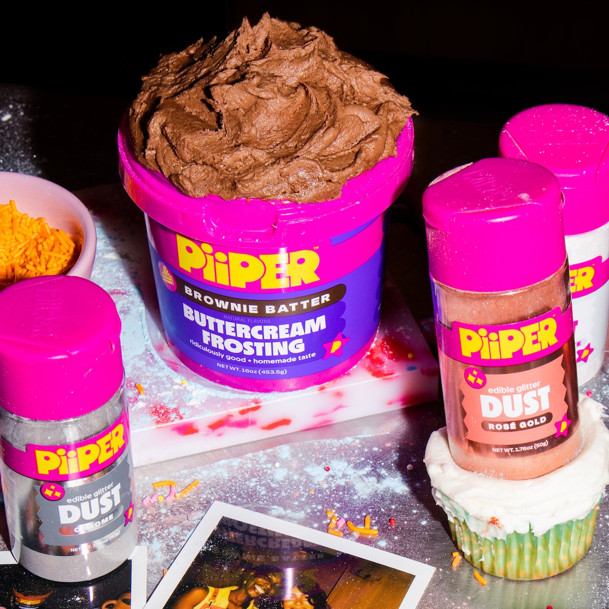PiiPER baking products displayed with chocolate buttercream frosting, edible glitter dust, sprinkles, and a decorated cupcake