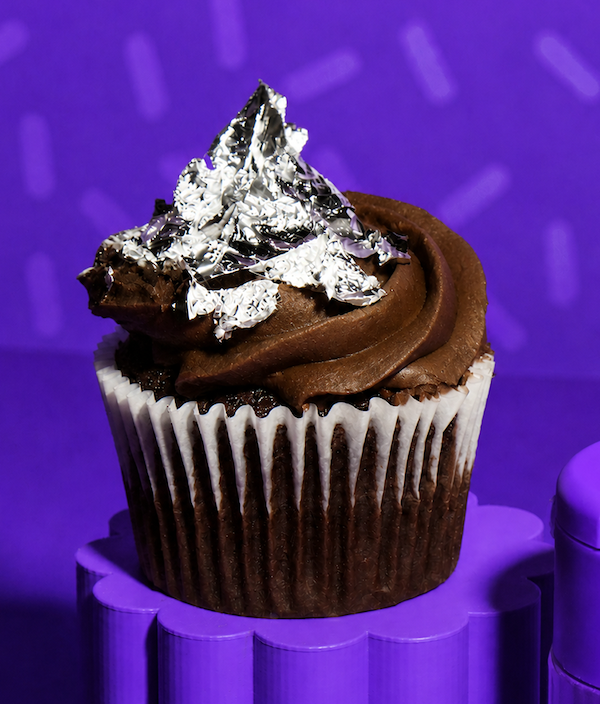 Front view of a chocolate cupcake topped with edible real silver flakes showcasing their reflective finish against a purple background